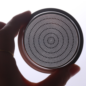 A precision 54mm filter basket being held up to the light, showing its uniform holes